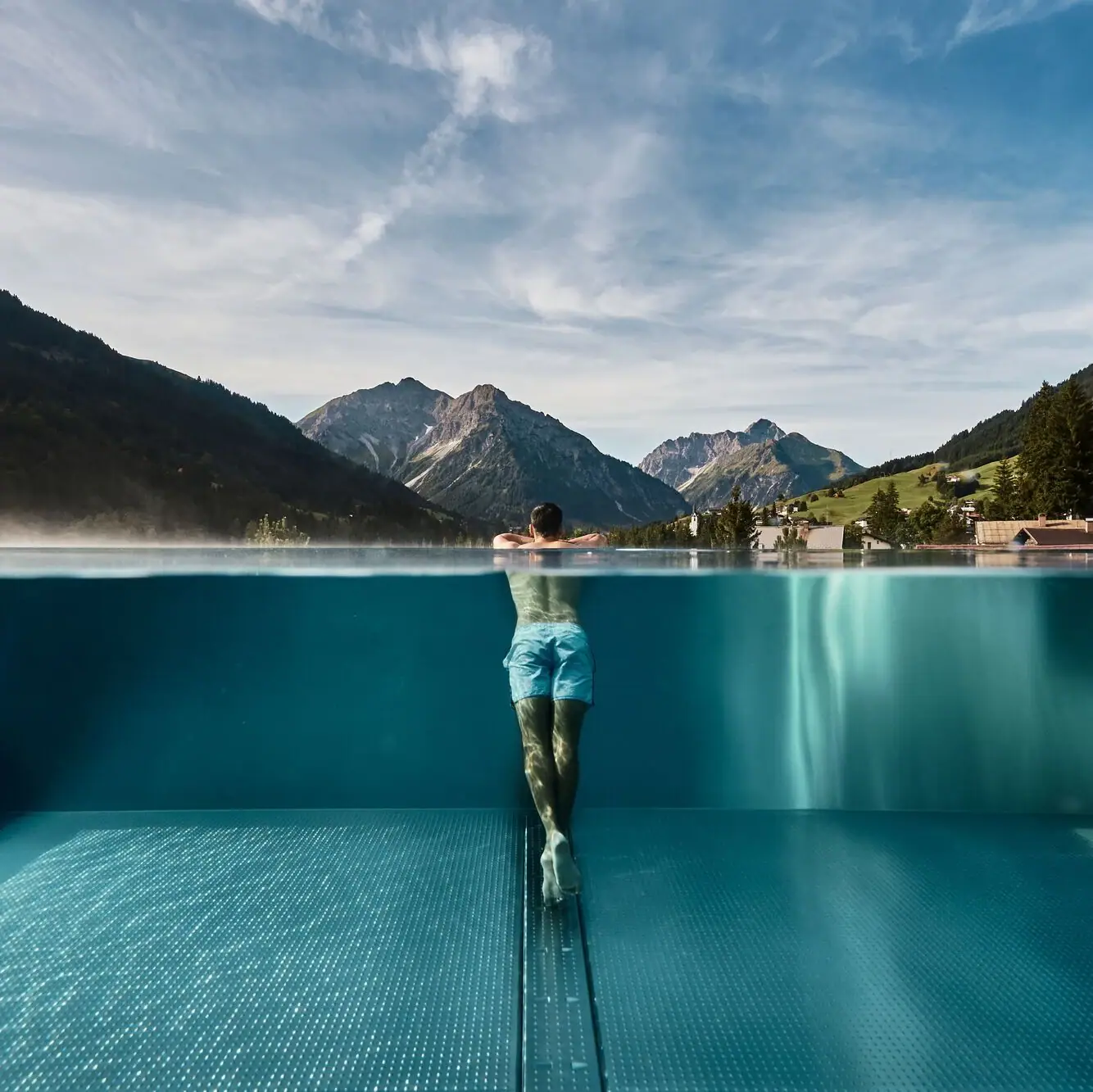 Ein Mann in einem Infinity Pool unter freiem Himmel mit Bergen im Hintergrund.
