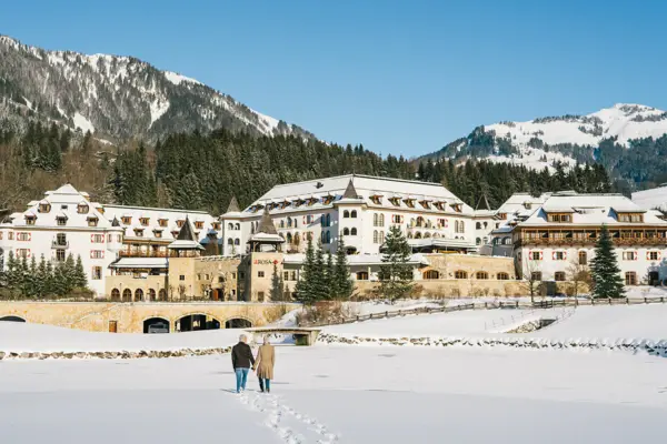 Ein großes, traditionelles Gebäude am Ufer eines Sees, umgeben von bewaldeten Hügeln, mit der aufgehenden Sonne im Hintergrund