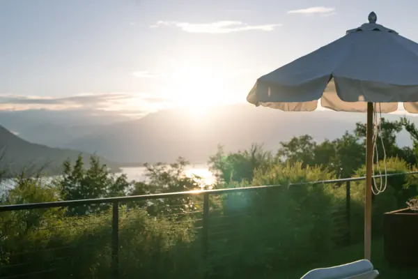 Weißer Sonnenschirm auf einer Terrasse mit Blick auf Gewässer und Himmel.