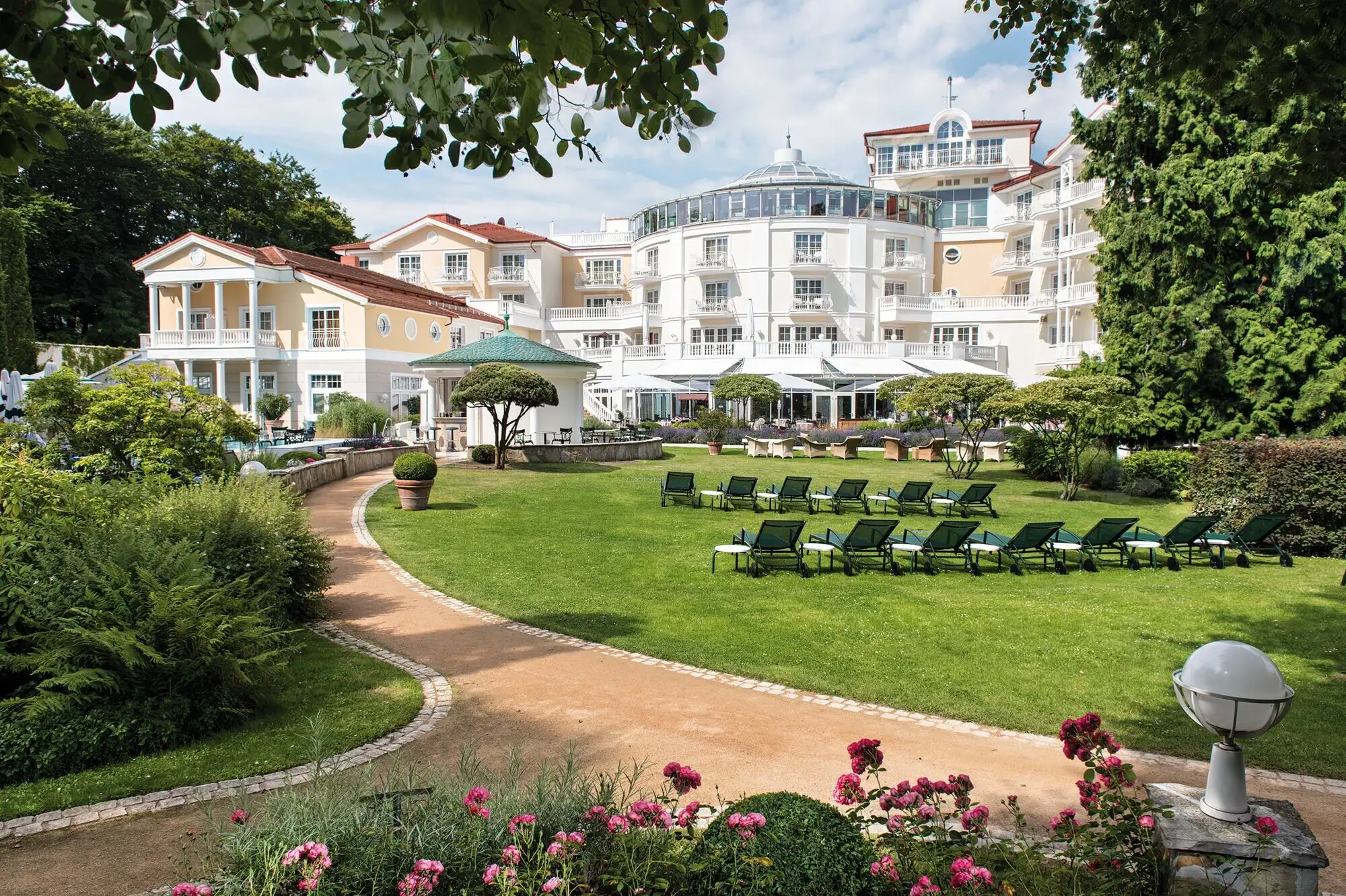 Liegestühle im Garten mit Rasen und einem Hotel sowie Bäumen im Hintergrund.