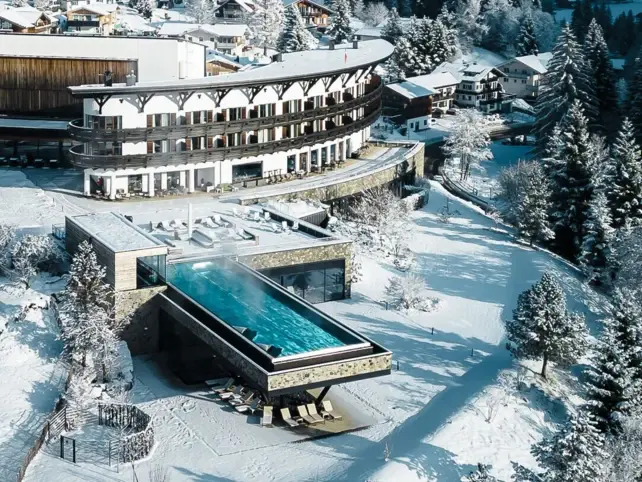 Gebäude mit Infnity-Pool im Schnee, umgeben von Bäumen und winterlicher Landschaft.