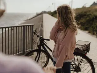 Eine steht seitlich vor einem Fahrrad an der Küste. 