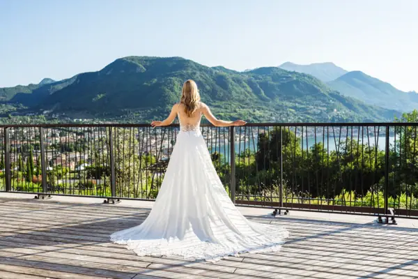 Eine Frau in einem weißen Kleid steht auf einem Deck mit Blick auf einen See.