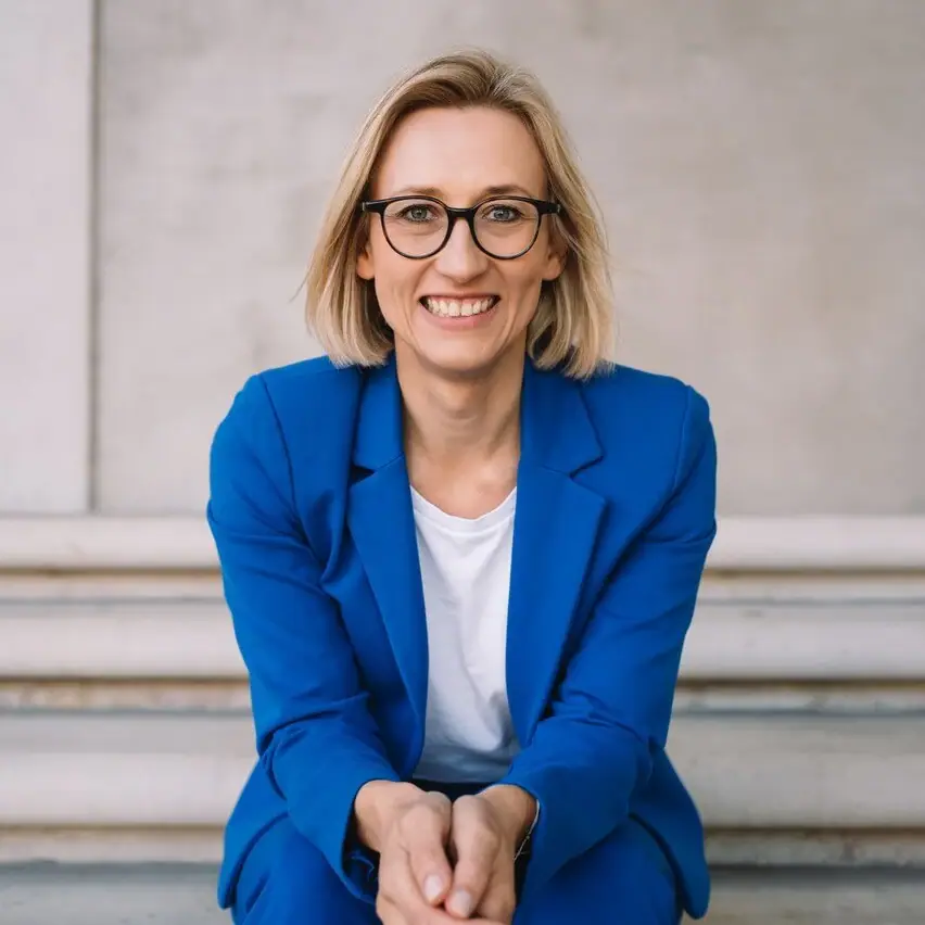 Eine Frau im blauen Anzug sitzt auf Stufen und lächelt.