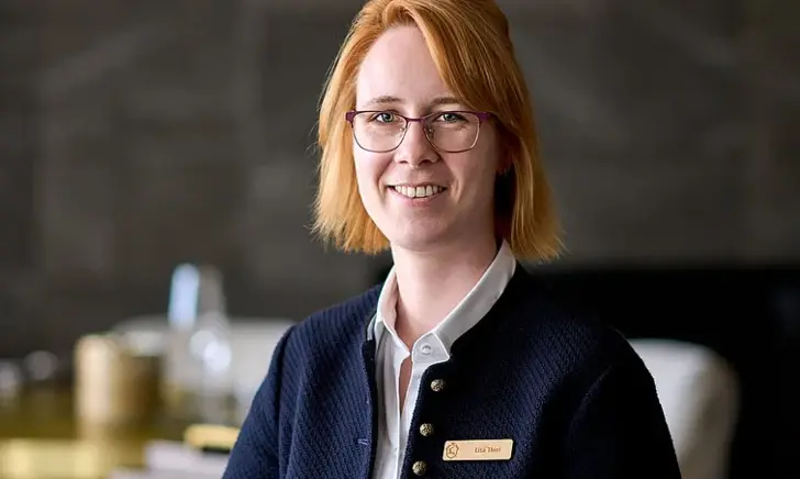 Woman with glasses and blue jacket smiling in a restaurant.