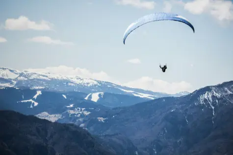 A paraglider hovers over a snowy mountain landscape.