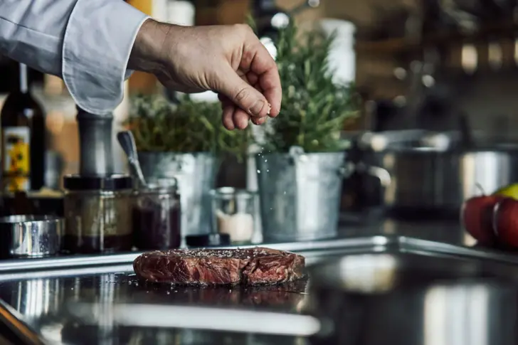 Eine Hand streut Salz auf ein Stück Fleisch.