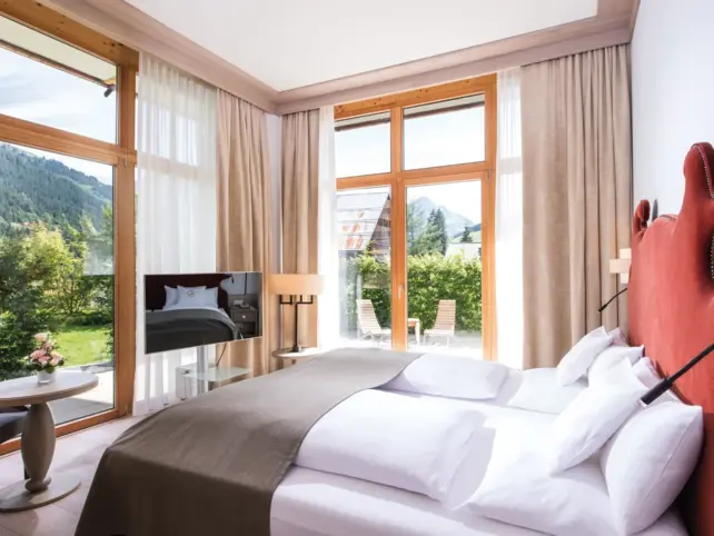 Inviting bedroom with a bed, a mirror and a chair with a view of a mountain landscape.