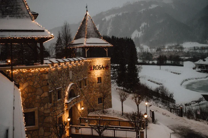 Das Hotel Kitzbühel abends erleuchtet, umgeben von schneebedeckter Winterlandschaft und Bergen. 