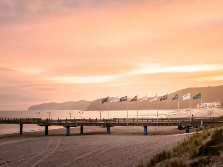 Brücke mit Flaggen bei Abenddämmerung, umgeben von Wasser und leicht bewölktem Himmel.