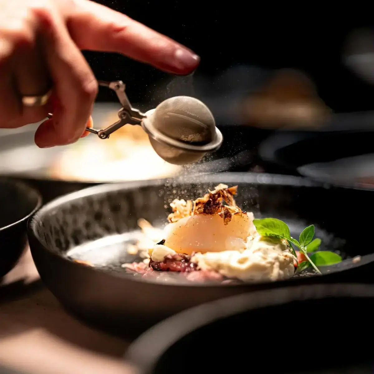 Eine Hand bestäubt ein Dessert auf einem Teller mit Puderzucker.