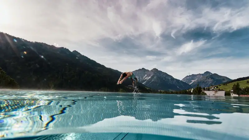 Eine Person springt in einen Pool mit Bergen im Hintergrund.
