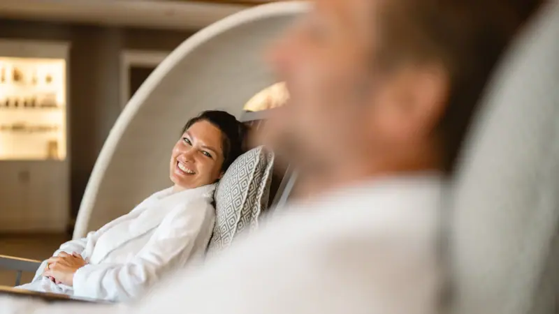 Eine Frau im Bademantel sitzt lächelnd auf einem Stuhl.