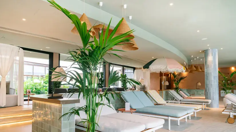 Un'area spa elegantemente accogliente, con piastrelle luminose, lettini per rilassarsi e piante decorative.