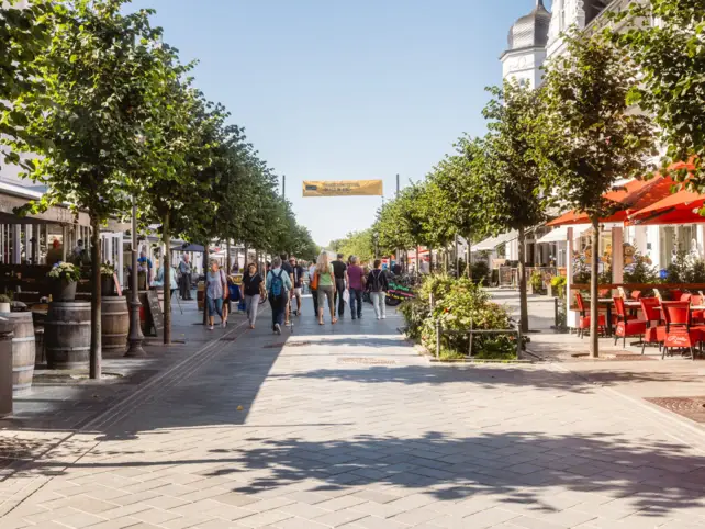 Eine Fußgängerzone in einer Stadt mit Menschen und vielen Geschäften.