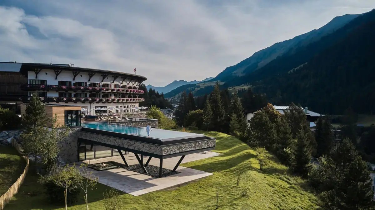 Ein Gebäude mit einem Infinity Pool auf Stelzen in der Mitte eingebettet in eine grüne Berglandschaft..