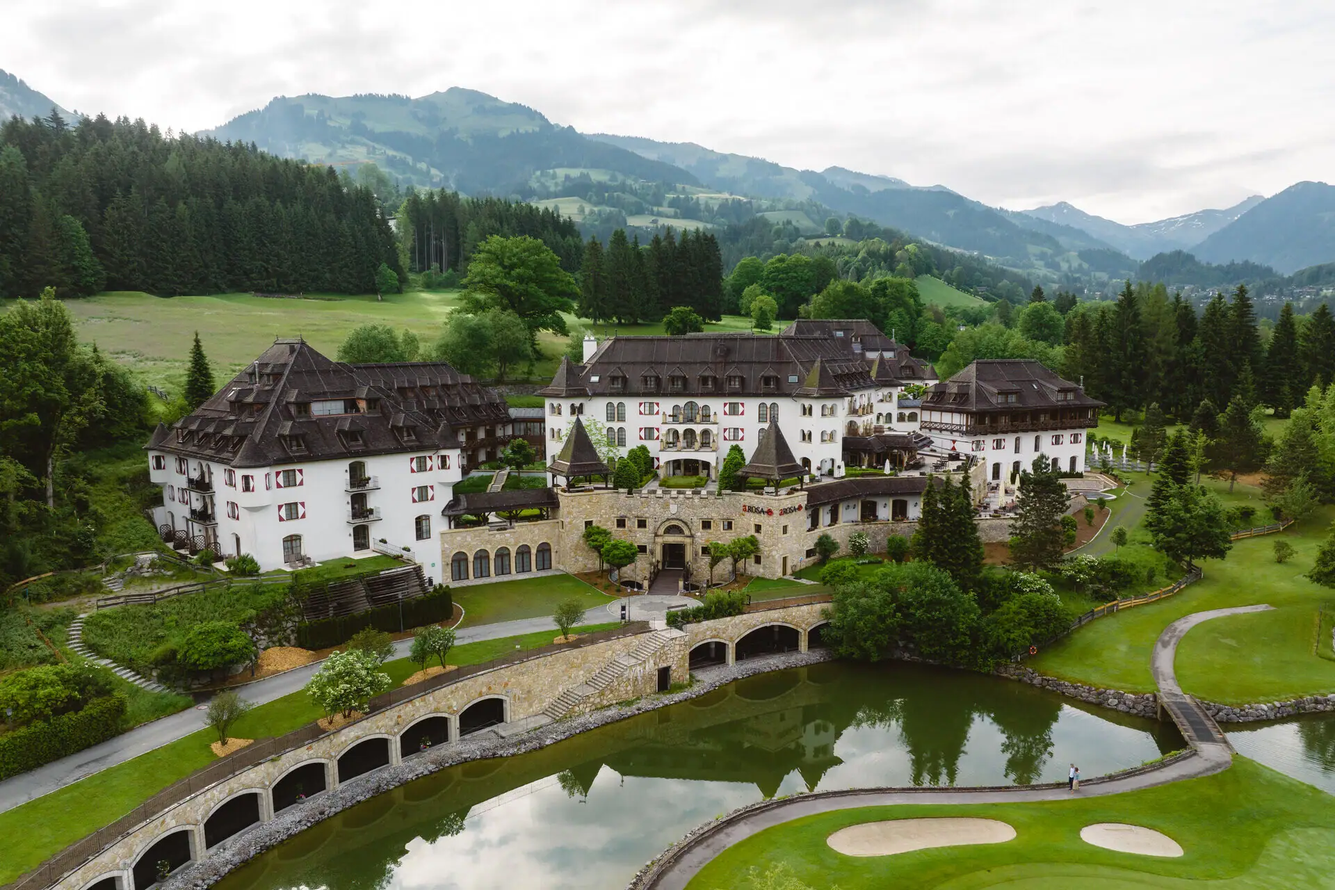 Das Schlosshotel Kitzbühel mit einem Teich und einem Golfplatz davor.