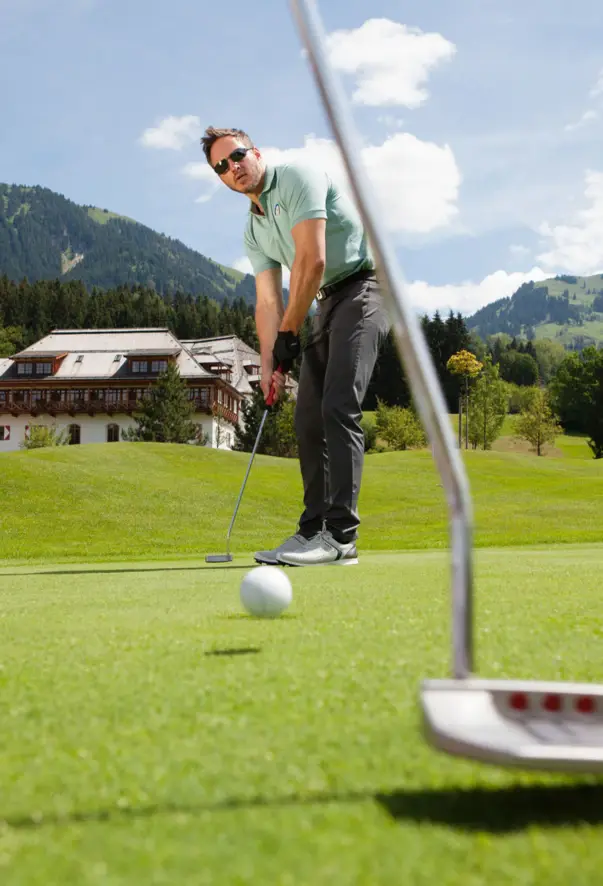Ein Mann visiert auf einem Golfplatz in grüner Umgebung einen Golfball zum Schlag an. 