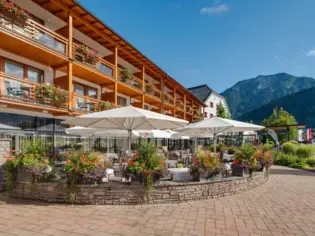 Das Fürstenhaus am Achsensee von außen fotografiert mit einer Terrasse und Sonnenschirmen umgeben von Bäumen und Pflanzen.