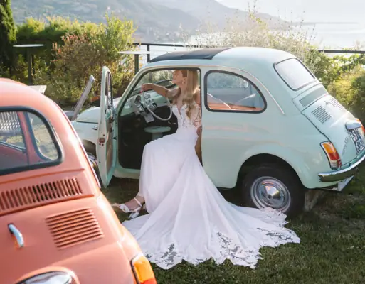 Eine Braut mit einem weißen  Hochzeitskleid sitzt in einem Fiat 500.