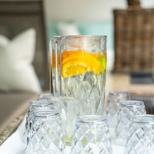 A pitcher of water with orange slices and glasses on a table.