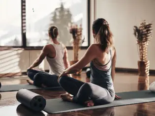 Zwei Frauen sitzen auf Matten in einem Zimmer und machen Yoga. 