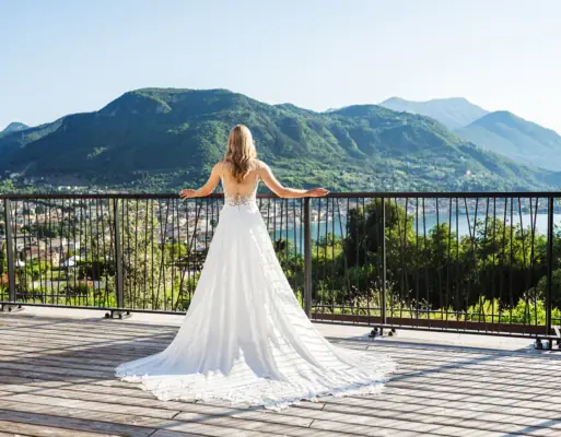 Eine Braut in einem weißen Kleid steht auf einem Balkon mit Blick auf den Gardasee.