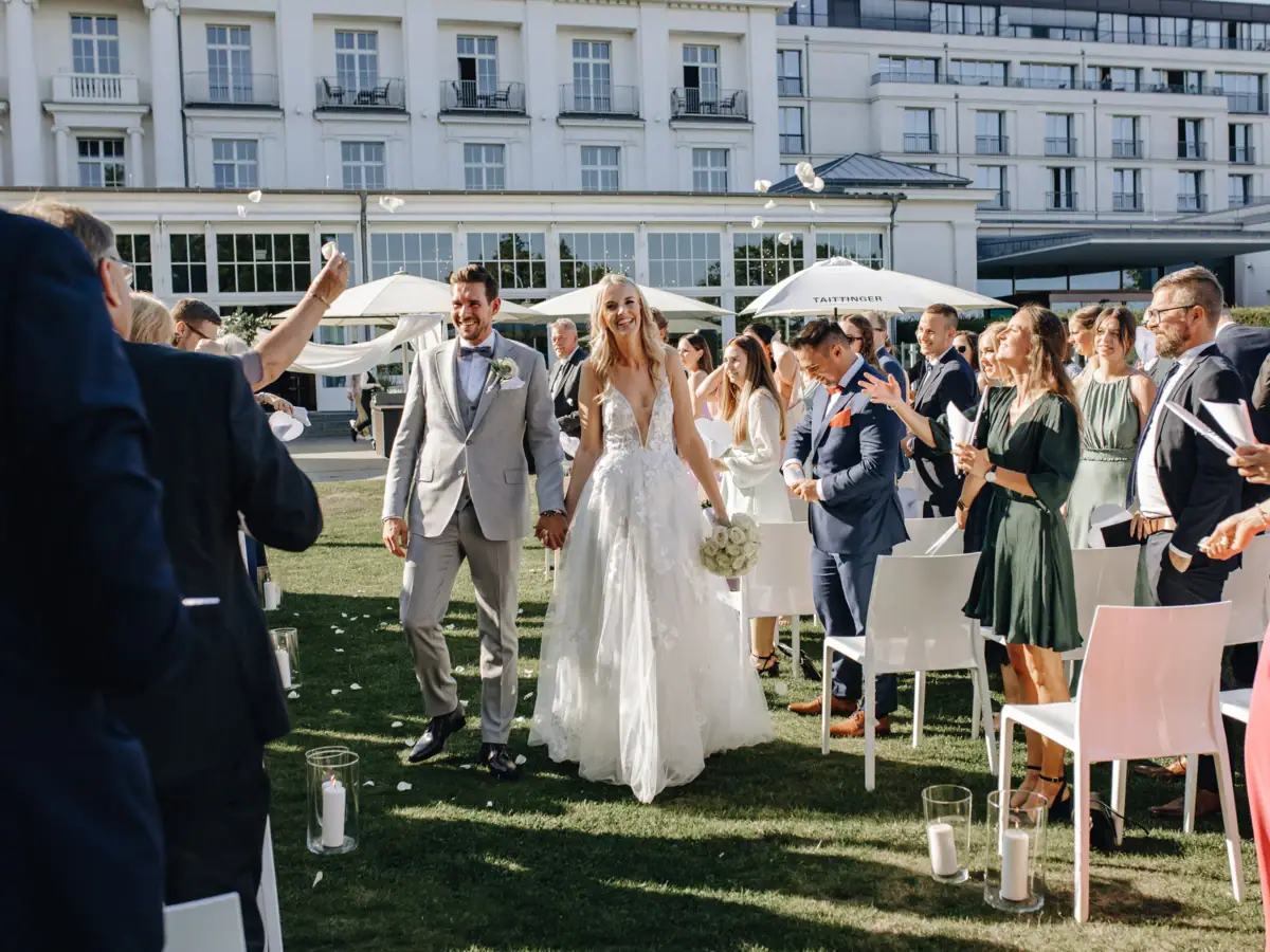 Hochzeitsfeier Travemünde Ein Mann und eine Frau im Hochzeitskleid gehen über einen Rasen.