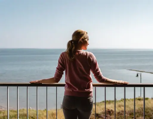 Doppelzimmer mit Meerblick Eine Frau steht auf einem Geländer mit Blick auf ein Gewässer.