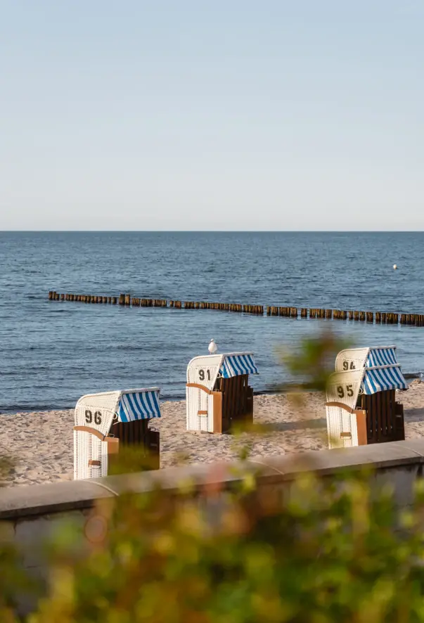 Strandkörbe mit gestreiften Markisen am Ufer eines Sees.