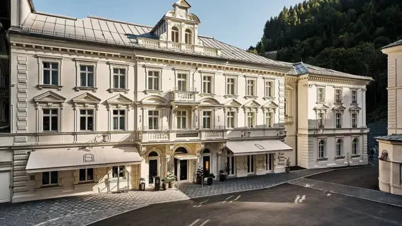 Ein helles, historisches Gebäude mit zwei Markisen steht auf einem Platz.