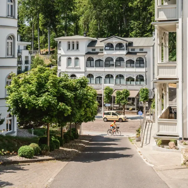 Eine Straße in einer Stadt mit weißen Häusern, ein paar grünen Bäumen und einem Radfahrer.