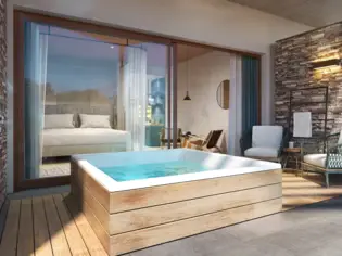 Luxurious spa suite with a large, rectangular wooden whirlpool in the foreground, filled with blue water that invites you to relax. Large window fronts provide a seamless transition to the sleeping area, where a cozy bed overlooks the pool. To the right of the suite is a stylish sitting area with two modern armchairs next to a wall of natural stone, creating a calming atmosphere. The suite combines modern comfort with natural elements.