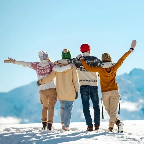 Vier Menschen stehen mit dem Rücken zur Kamera im Schnee und Blicken in die verschneite Berglandschaft.