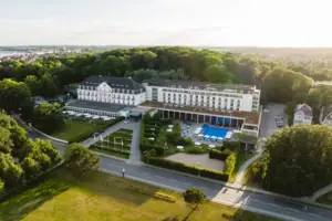 A-ROSA Travemünde Ein großes weißes Gebäude mit einem Pool und Bäumen.
