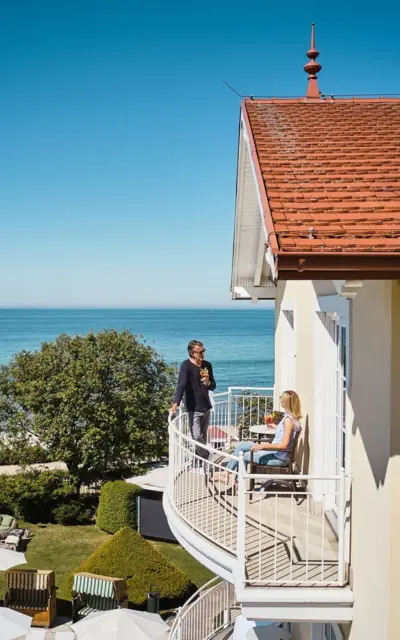 Zwei Personen auf einem Balkon mit Blick auf einen Strand.