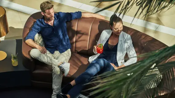 Ein Mann und eine Frau sitzen mit ihren Begrüßungsgetränken in der Lobby auf einem Sofa. 