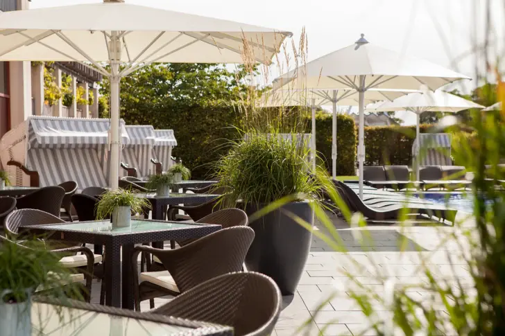 Ein Hotelaußenbereich mit vielen Sitzmöglichkeiten, Strandkörben und einem Außenpool, um den Liegen stehen. 