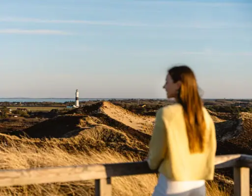 Eine Frau steht an einem Zaun und blickt auf einen Leuchtturm.