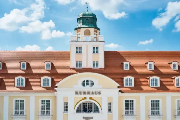 Außenansicht des A-ROSA Kurhaus Binz mit hellen Fassaden, einem roten Dach und Turm. 