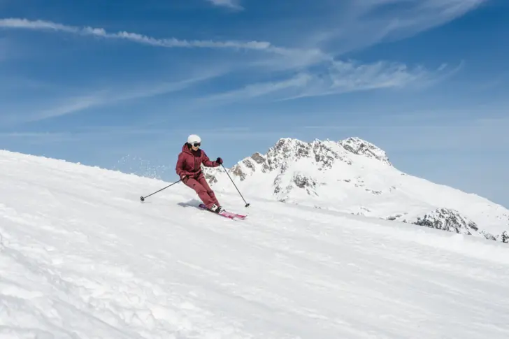 Person beim Skifahren auf verschneiter Piste in einem Skiort.