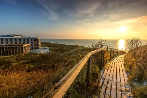 Holzsteg führt zu einem Strand mit Gebäude im Hintergrund.
