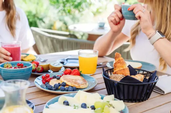 Frau hält eine Tasse Kaffee an einem Frühstückstisch mit vielen Tellern mit Essen.