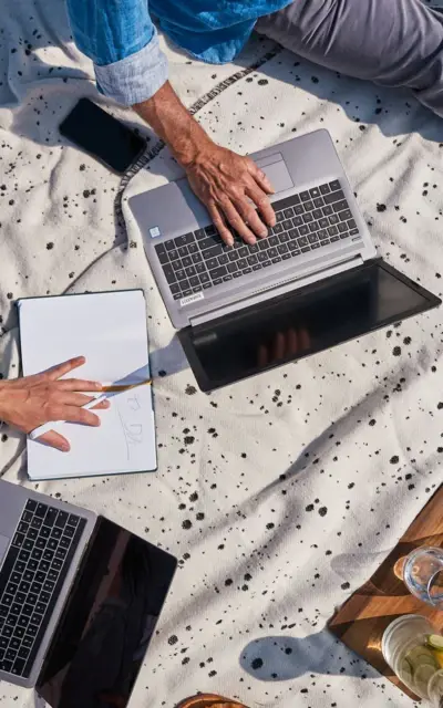 Person hält eine Tasse Kaffee und sitzt an einem Tisch mit Laptop.