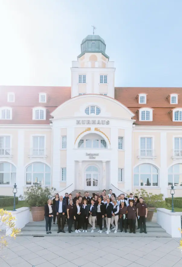 Eine Lobby Ansicht von zwei Etagen. Die obere Etage ist von einem schwarz goldenen Zaun umrandet. An den Wänden hängt eine Vielzahl an unterschiedlichen Spiegeln und es stehen verschiedene Sitzmöglichkeiten verteilt. 